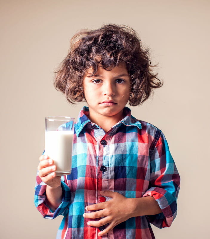 a child holding a glass of milk with their hand on their stomach