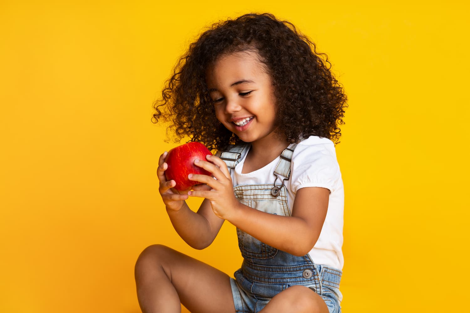 A child smiling whilst holding an apple