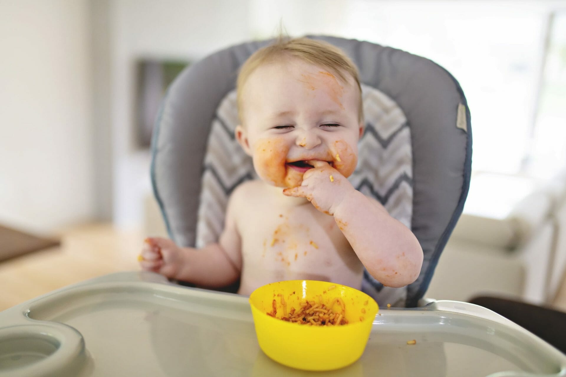 a baby eating food in their highchair and smiling
