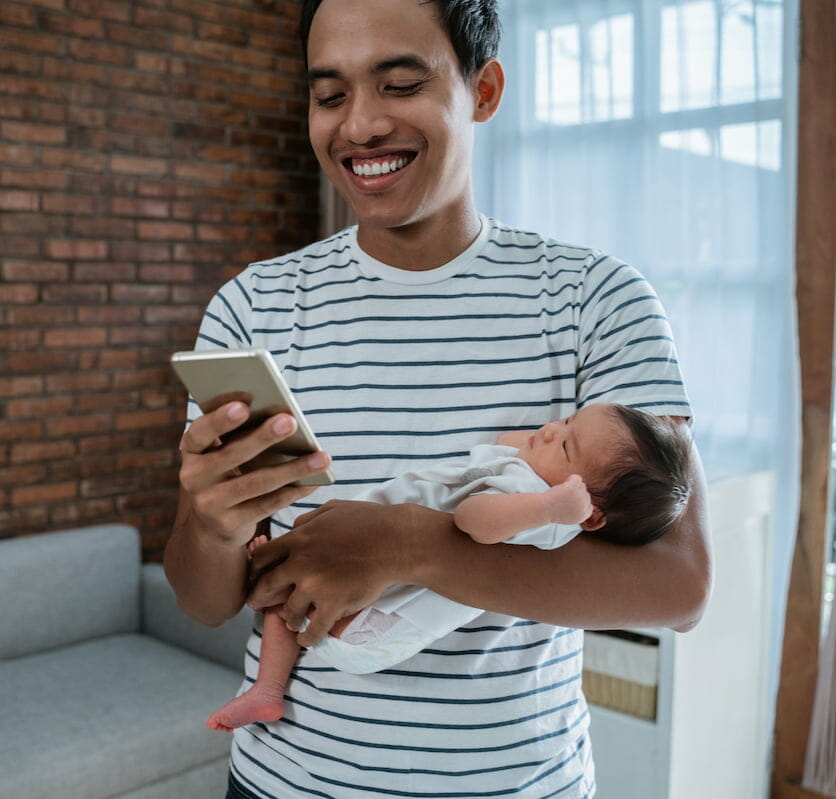 a father holding his newborn whilst using his phone