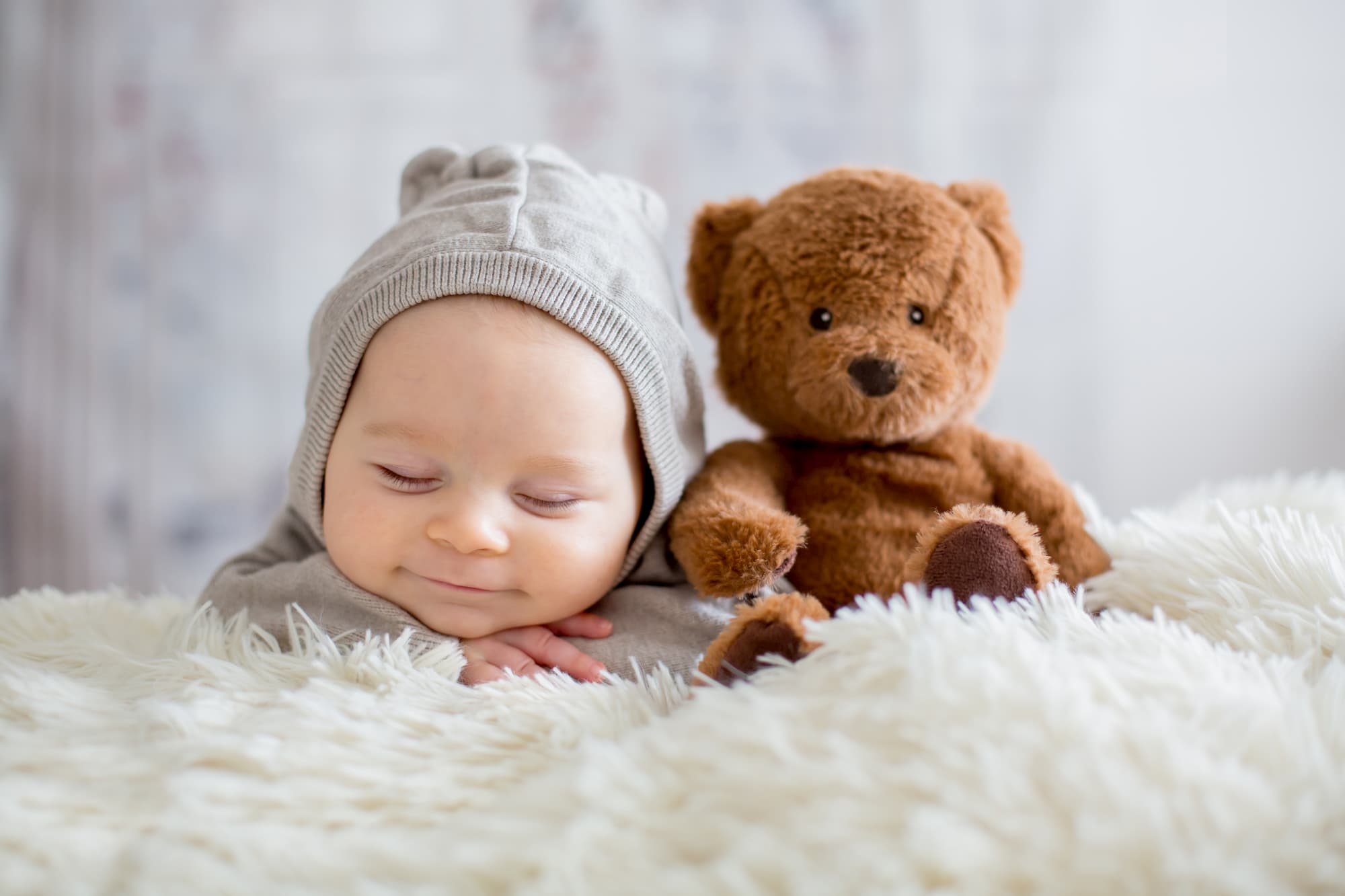A smiling baby lying on a rug with their cuddly toy