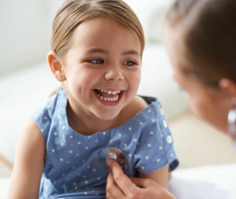 A smiling girl being examined with a stethoscope