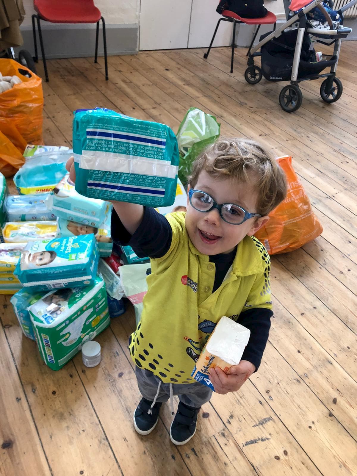 A child with glasses holding up a packet of nappies
