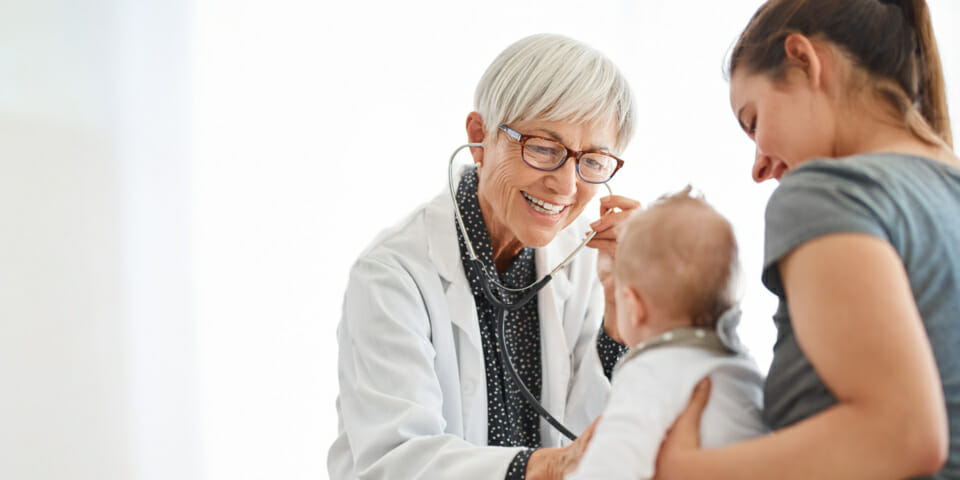 a doctor smiling whilst assessing a baby with a stethoscope