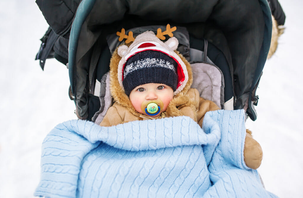 Babywith a pacifier in a buggy at a winter day.